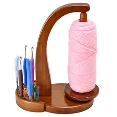 a pink ball of yarn sitting on top of a wooden stand next to crochet hooks