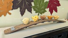 a wooden serving board with different types of snacks on it and leaves hanging from the wall