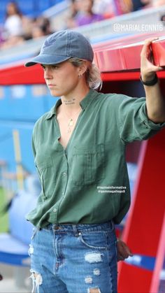 a woman in ripped jeans and a baseball cap is holding onto a red bench at a football game