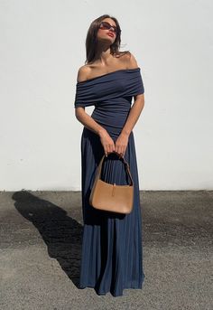 a woman in a blue dress is holding a brown bag and posing for the camera