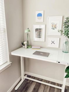 a white desk topped with a laptop computer next to a potted plant and framed pictures