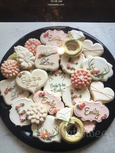 a black plate topped with cookies covered in frosting and decorated like flowers, hearts, and words