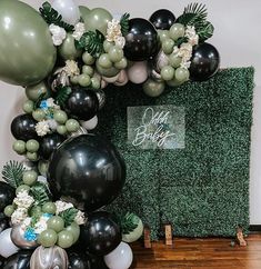 black, white and green balloon arch with greenery