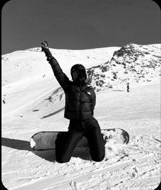 a snowboarder sitting in the snow with his arms up and one hand raised