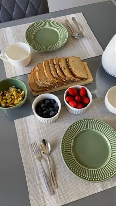 a table topped with plates and bowls filled with fruit next to bread on top of a cutting board