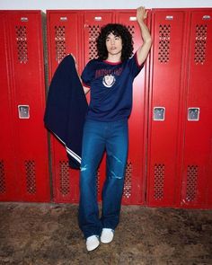 a woman standing in front of lockers holding up a blue shirt and black jacket