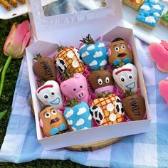 an open box filled with lots of decorated cookies on top of a blue and white checkered table cloth