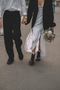 a bride and groom holding hands walking down the street with other people in the background