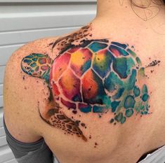 the back of a woman's shoulder with a watercolor turtle tattoo on it