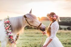 a woman in a wedding dress is petting a horse with a flower crown on its head