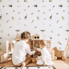 two children playing with wooden toys in front of a wallpapered nursery room area