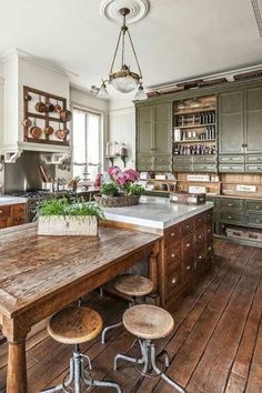 an old fashioned kitchen with wooden floors and green cabinets is pictured in this image, there are stools at the center of the table