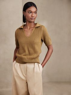 a woman standing with her hands on her hips wearing tan pants and a brown sweater