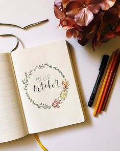 an open notebook with the words hello october on it next to some pencils and flowers