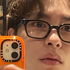 a man with glasses is holding up an orange case to take a selfie in front of his face