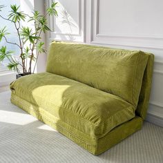 a green couch sitting on top of a white floor next to a potted plant