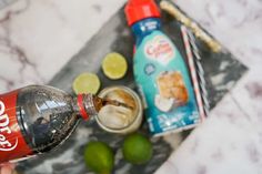 a person is holding a coke bottle with ice and limes around it on a marble tray