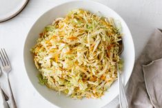 a white bowl filled with coleslaw on top of a table next to silverware