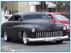 an old fashioned car is parked on the street in front of some other classic cars