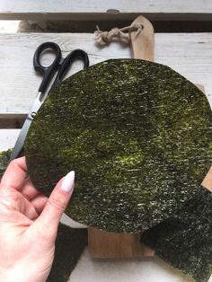 someone is cutting moss on top of a piece of wood and scissors are next to it