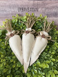 three burlap heart shaped ornaments on top of green leaves with the words urban barn