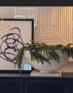 a plant in a white vase on top of a black table next to a framed art piece