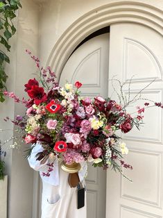 a woman holding a large bouquet of flowers in front of a white door with an arched doorway