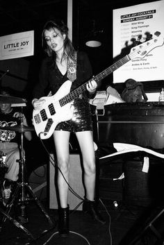 black and white photo of woman playing guitar in front of microphones with band members behind her