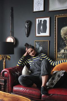 a woman sitting on top of a red couch in a living room next to pictures