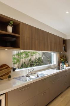 a modern kitchen with wooden cabinets and white counter tops is pictured in this image, there are plants on the window sill above the sink