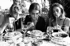 three women sitting at a table with plates and wine glasses in front of their faces