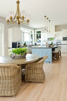 a dining room table and chairs in front of a kitchen with white cabinets, blue island and gold chandelier