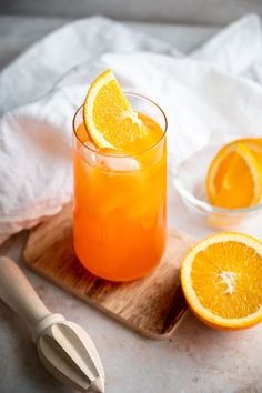 an orange juice in a glass next to sliced oranges on a wooden cutting board