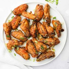 chicken wings with sesame seeds and green onions on a white plate, ready to be eaten