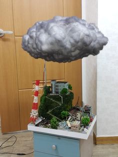 a cloud is hovering over a small model house on a dresser in a room with wood paneling