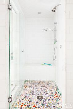 a white tiled bathroom with a shower stall and flowered floor tiles on the walls