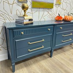 a blue dresser with gold handles and two pumpkins on top