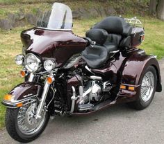 a maroon motorcycle is parked on the side of the road in front of some grass