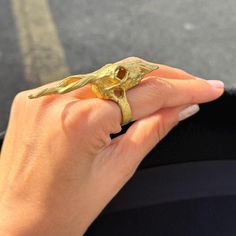 a woman's hand holding a gold ring with a lizard on it, in front of a street