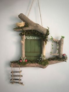 a welcome sign hanging on the wall next to a tree branch with flowers and vines