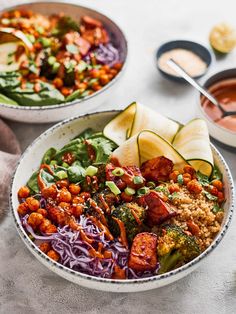 two bowls filled with different types of food on top of a white table cloth next to dipping sauces