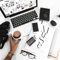 a person holding a cup of coffee in front of a laptop on a table with other items