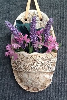 purple flowers are in a basket hanging on the wall with leather handles and straps around it