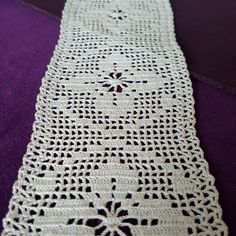 a white crocheted table runner sitting on top of a purple cloth