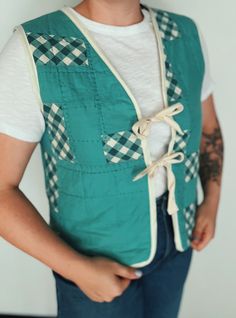 a man wearing a green vest and white t - shirt is standing with his hands in his pockets