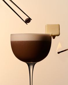 a chocolate drink is being poured into a wine glass with two sticks sticking out of it