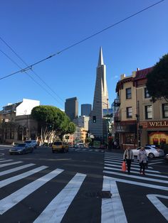 two people crossing the street in front of a tall building with a steeple on it