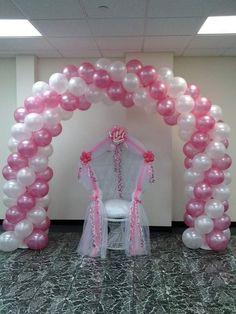 an arch made out of balloons with a chair in the middle and pink ribbons around it