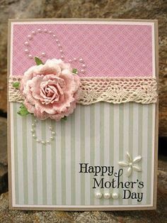 a mother's day card with a pink rose and pearls on the edge, sitting on some rocks