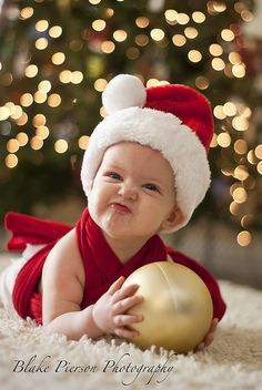 a baby wearing a santa hat and holding a golden ball